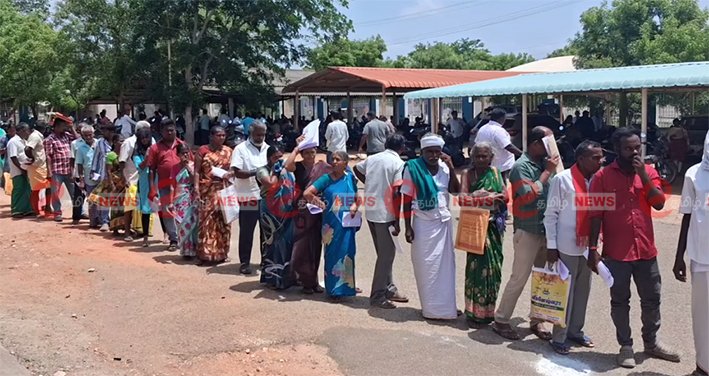 A large crowd of people, including senior citizens, standing in a long queue under hot sun outside Karur Collector office with no ambulance facility in June 2026.